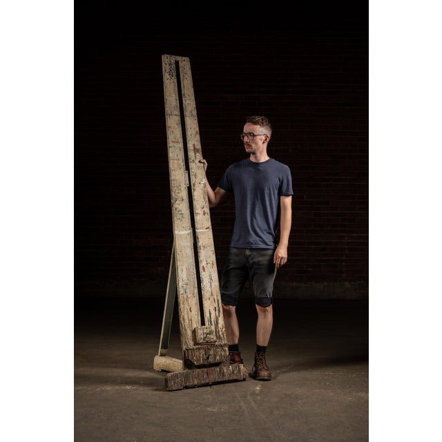 Tall studio easel in wood with iron fittings and an adjustable sliding clamp for large-format canvases. Standing over...