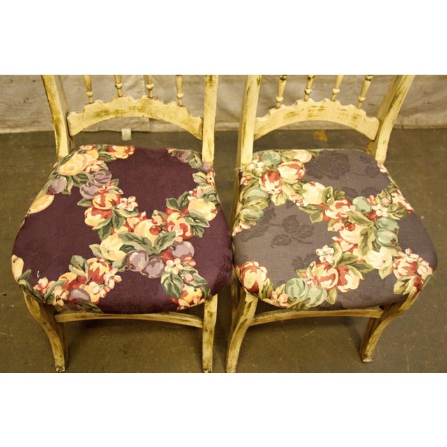 Pair of wooden French Country style chairs with cream coloring complemented by a graceful curving silhouette and a homey...