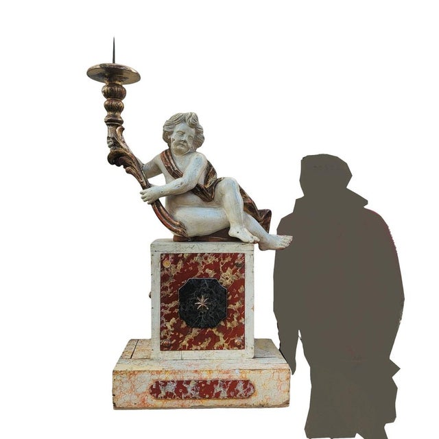Large lacquered and gilded wooden sculpture of a seated putto, holding a candlestick at arm's length. He sits on a later,...