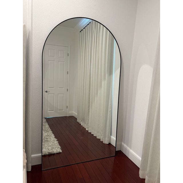 Stunning full-length arched floor mirror by Renwil featuring a slim black iron frame and clean architectural silhouette....