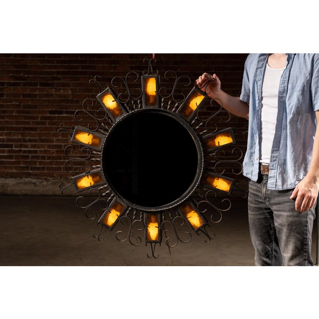 A dramatic circular illuminated mirror framed in hand-wrought iron, designed in a bold sunburst configuration. The mirror...