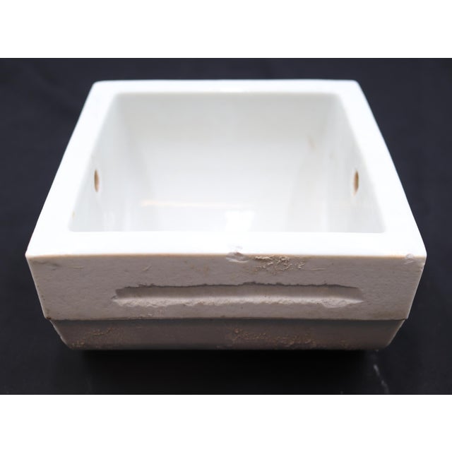 This flush mount toilet paper holder is made of white porcelain over ceramic with a square shape and curved interior back....