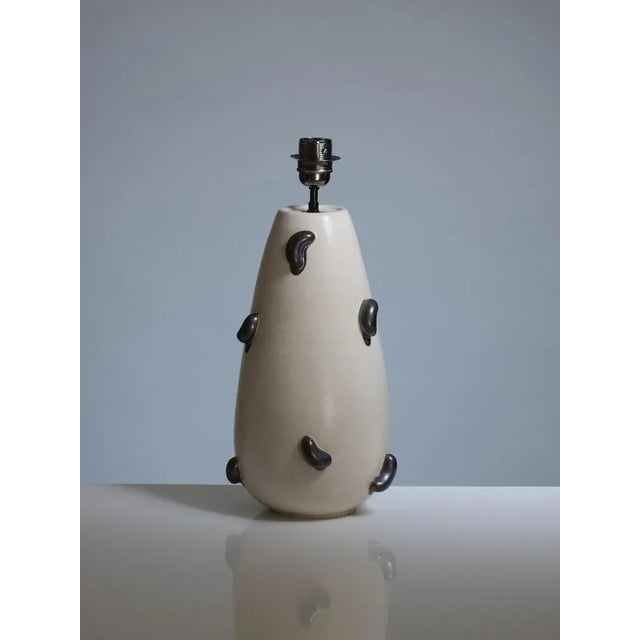 This ceramic lamp exudes a unique and organic design with its teardrop-shaped base, crafted from smooth, creamy beige...