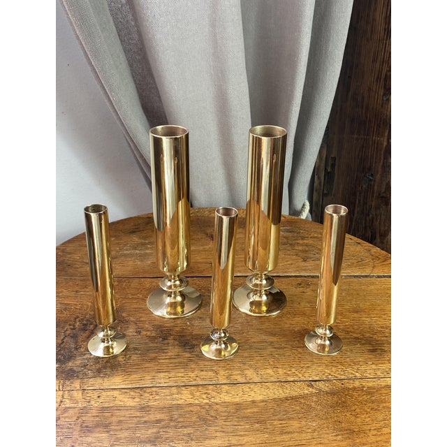 An elegant set of cylindrical, gilded brass candlesticks and bud vases of varying heights, mounted on round bases. These...