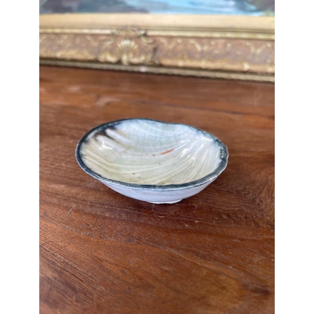 This vintage Japanese pottery dish is crafted in the form of a clam shell and features a pale celadon glaze with fine...