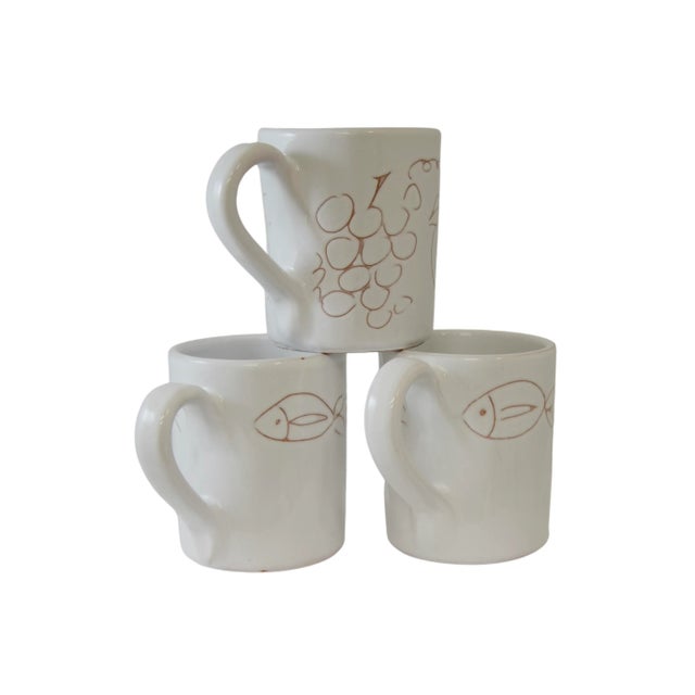 Set of three large vintage pottery mugs in white with incised fish, fruit and flowers. Marked underside. Light wear with...