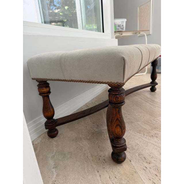 Traditional English Carved Oak Bench with a tufted beige suede seat and Brass Nailhead Trim.
