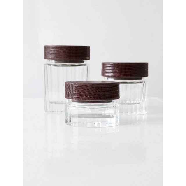 his is a set of three vintage cut glass jars with leather lids. The graduated set has a ribbed pattern with reptile...