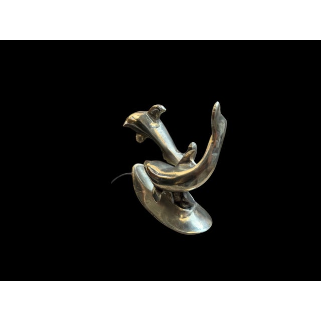 A handmade brass dolphin sculpture with two intersecting dolphin forms rising from a shell-like base. The composition...