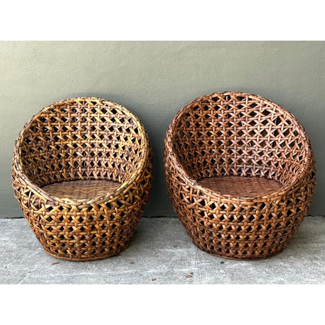 Sculpted into a rounded barrel silhouette, this pair of mid-century lounge chairs is crafted from thick woven rattan with...