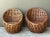 Sculpted into a rounded barrel silhouette, this pair of mid-century lounge chairs is crafted from thick woven rattan with...