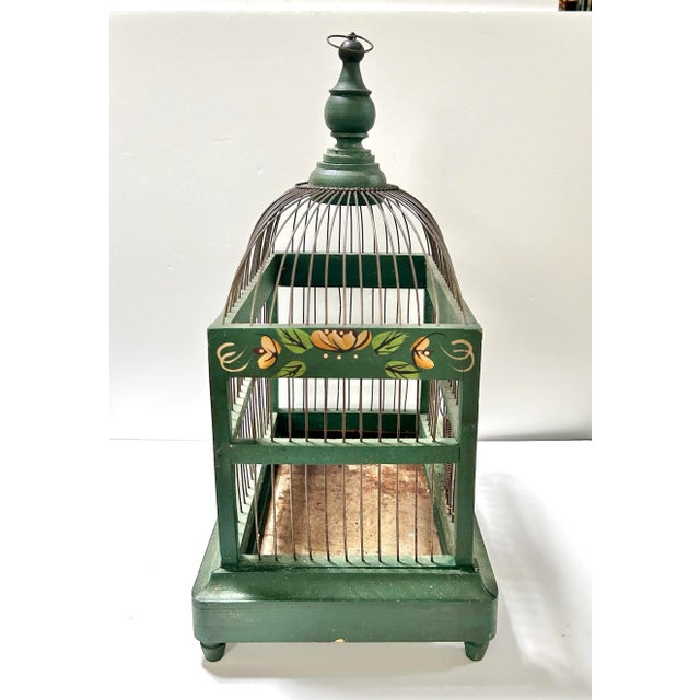 An early 20th-century decorative wire birdcage featuring a domed top and hand-painted green wooden base adorned with...