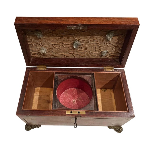 A regency tea caddy made of rosewood inlaid with brass. Bronze dore feet are a winged lion with flowers and fruit. A...