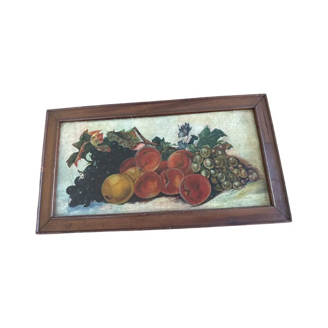 An appealing early 20th century fruit still life oil painting presented in its original wood frame. Grapes, peaches, and a...