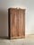 Antique pine cabinet with a hand-carved scroll crest and paneled doors, the surface showing wide board construction with...
