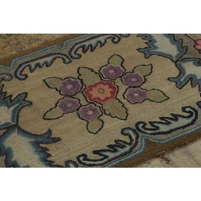 This antique 2x4 hooked rug, circa 1920–1929, displays a floral medallion framed by scrolling foliate motifs and stylized...