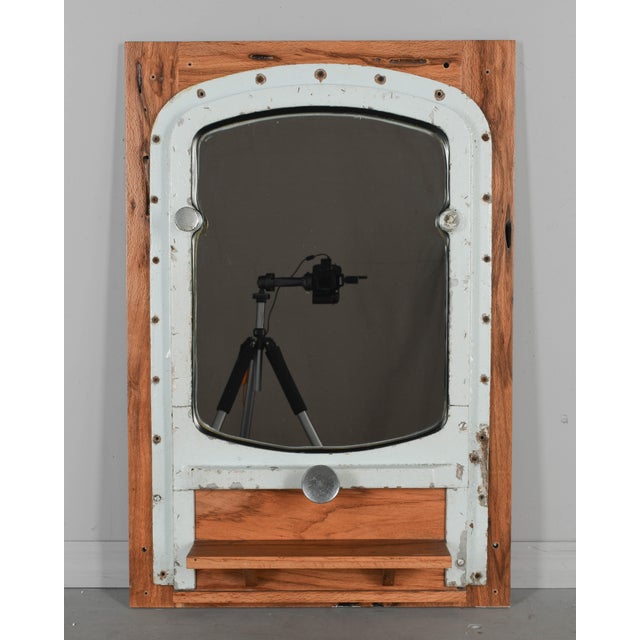 A rustic salvaged ship's portal repurposed into a wall mirror. Mounted to an oak frame with a small ledge or shelf. Pale...
