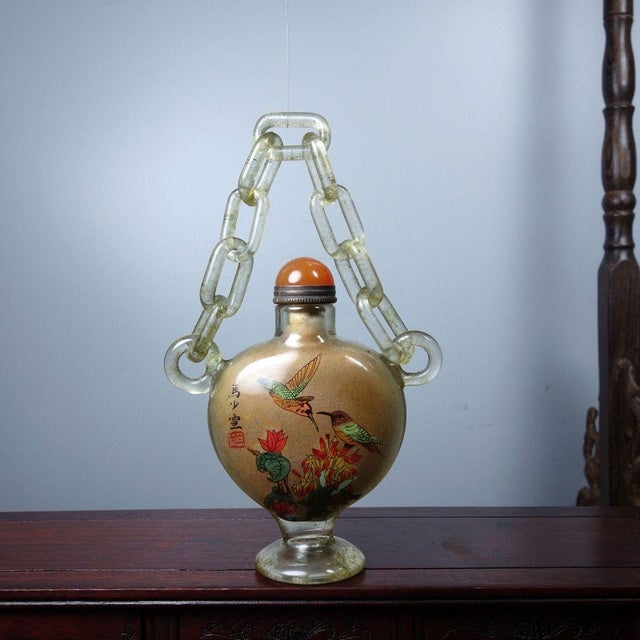 This distinctive snuff bottle is crafted from clear glass and features an intricate hand-painted interior scene. The...