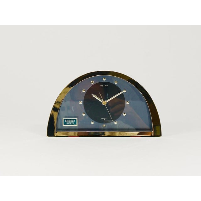 A decorative Hollywood Regency desk/table/mantel clock from the 1980s. It features a brushed brass housing with a mirror-...