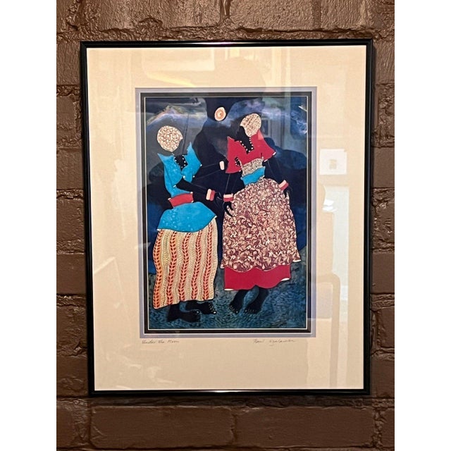 Framed art print titled "Under the Moon" by Ugandan artist Paul Nzalamba. Features two women under a full moon dressed in...