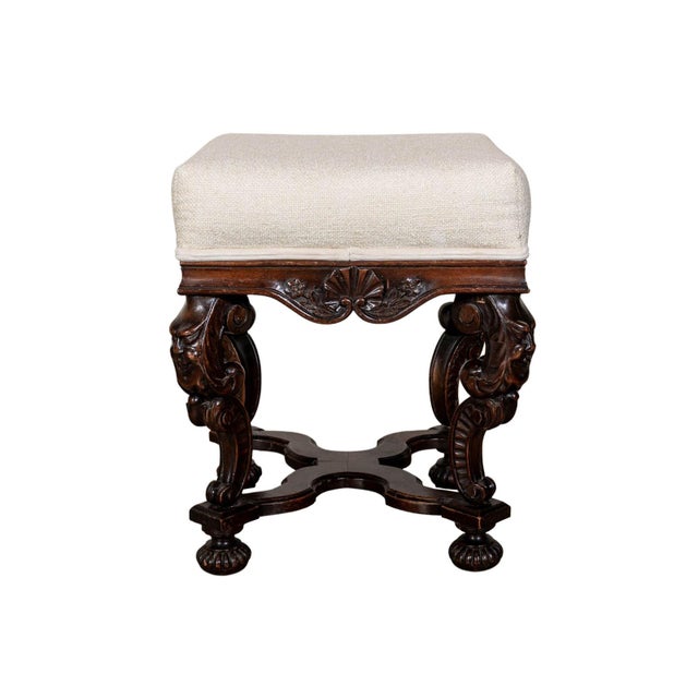 Upholstered stool with bun feet. Grotesque leg carvings. Apron with floral motifs.