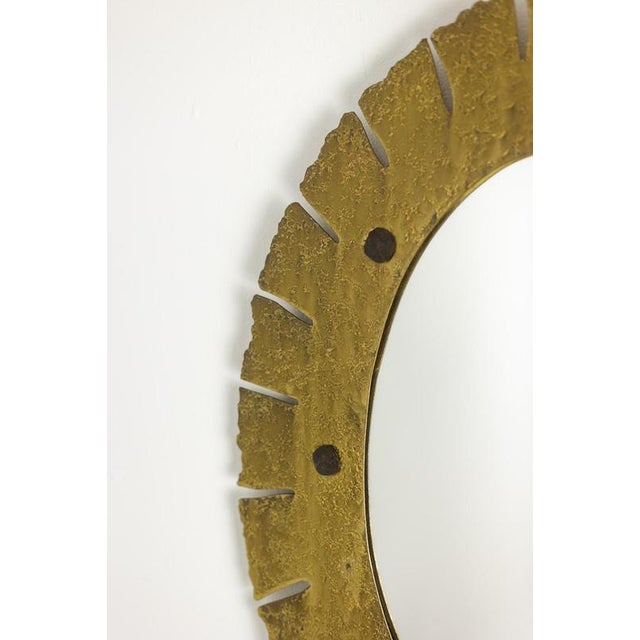 Elliptical mirror in hammered and gilded brass, with a cut edge decorated with 8 grey iron cabochons. A work of art by a...
