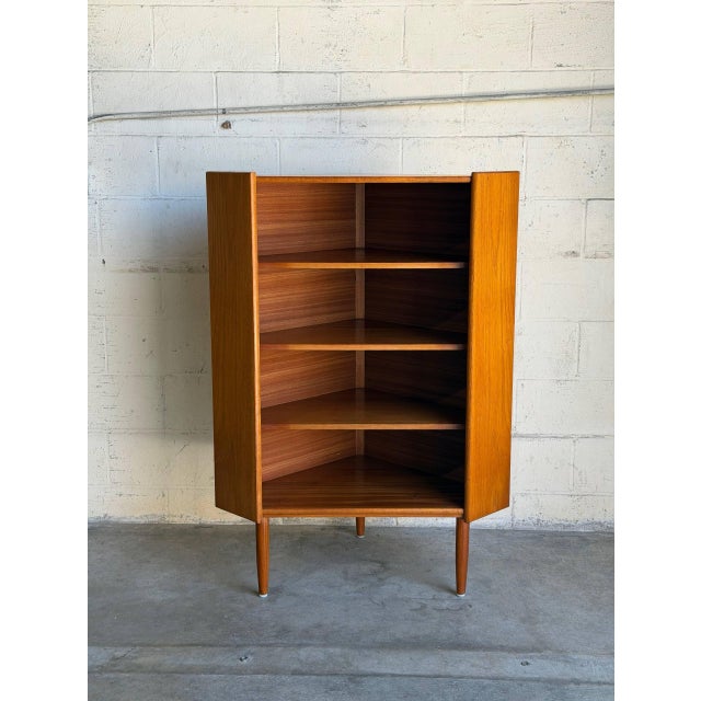 This teak corner cabinet uses an angular footprint to fit neatly into a room corner. Three open shelves and an elevated...