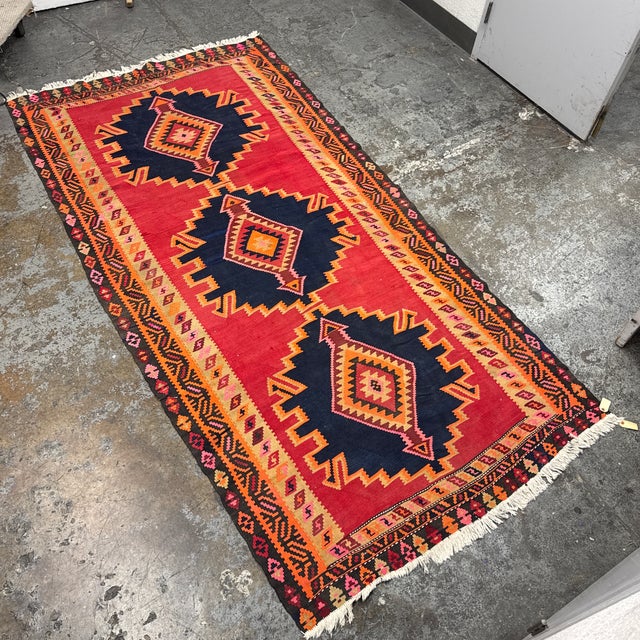 Design Plus Gallery presents a Vintage Handwoven Kilim Runner. This flatweave rug has a red field with three large navy...