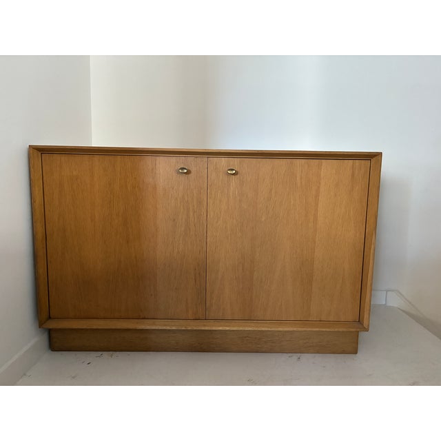 Modern light oak cabinet on a plinth base, featuring its original brass knobs with a gorgeous patina. This vintage light...