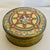 An interesting early 20th century round metal box featuring a lady holding a cake and surrounded by an intricate...