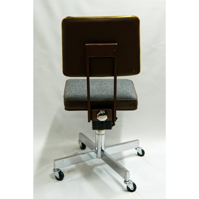Industrial rolling office chair manufactured by United Chair, featuring a sturdy metal frame, vinyl and fabric upholstery,...