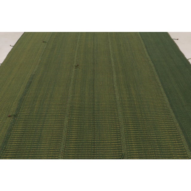 Handwoven in wool, this 8x12 Rez Kilim showcases tonal bands of olive, moss, and forest green arranged in a quiet linear...