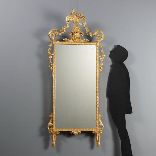 Neoclassical-style mirror in carved and gilded wood. The carved cymatium features a central face surmounted by an eagle...