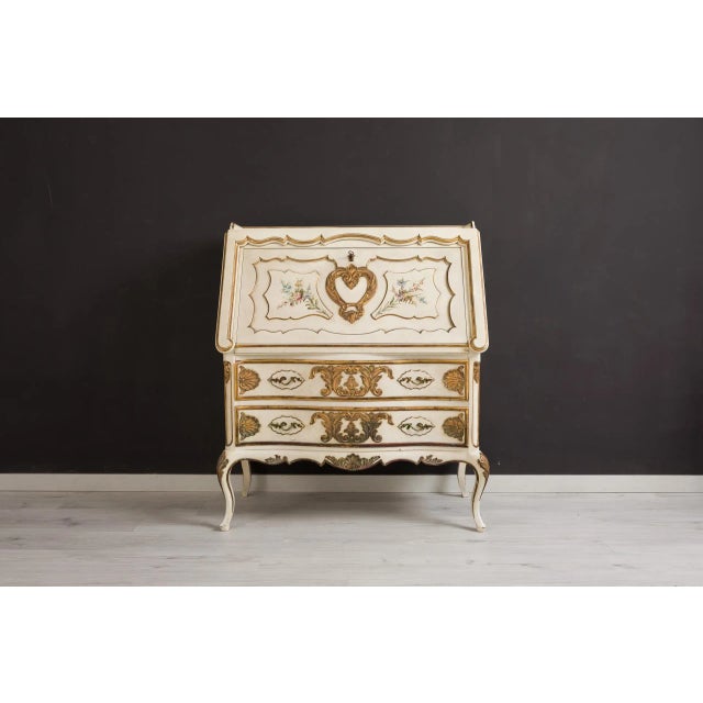 Elegant vintage secretaire featuring three drawers and a drop-down writing flap. The piece is richly decorated with hand-...
