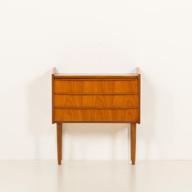 This small teak dresser was made in Denmark in the 1960s. It features three drawers with integrated solid teak sculptural...