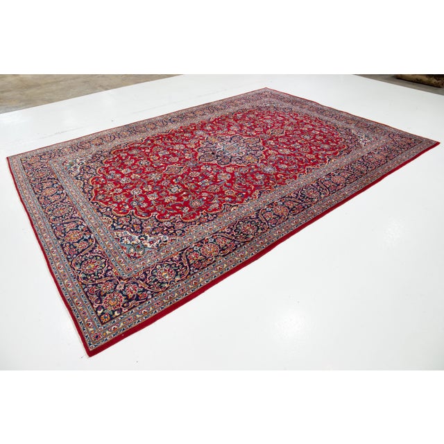 This vintage Kashan hand-knotted Persian wool rug features a striking red background adorned with a rosette motif and...