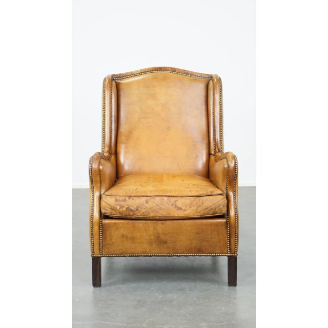 Comfortable and cognac-colored vintage sheep leather armchair with a high back and a correct finish with decorative nails....