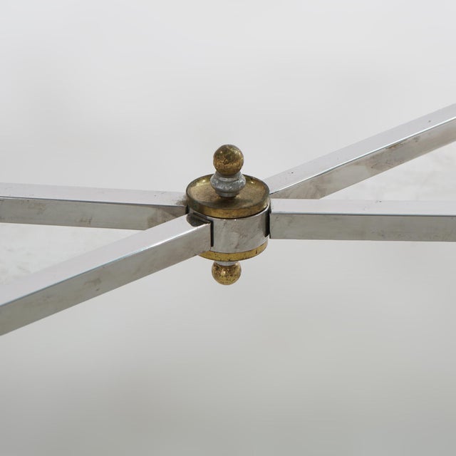 A Mid Century Modern Hollywood Regency coffee table offers glass top over chrome base having stylized splayed legs...