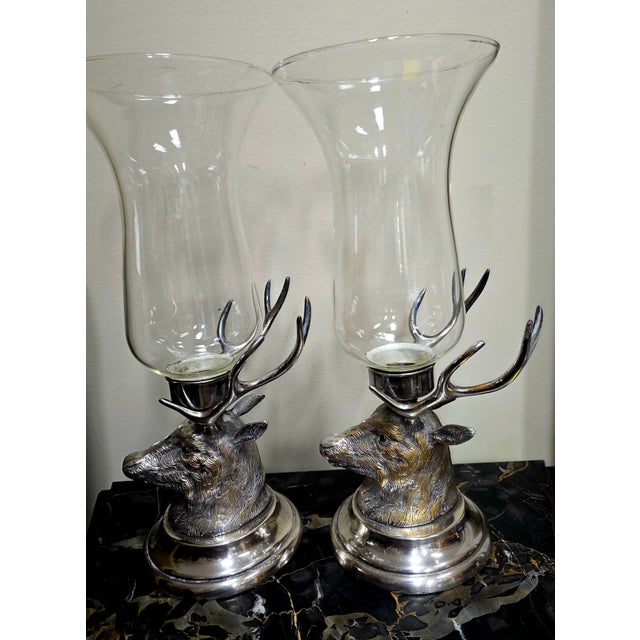 The Carole Stupell Set of 2 Silverplate Stag Head Hurricane Lamps is a traditional and decorative set of candle holders in...