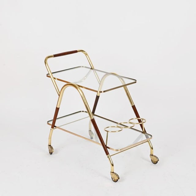 Spectacular and unique Italian bar trolley in solid brass, walnut wood and crystal glass. This stylish mid-century serving...