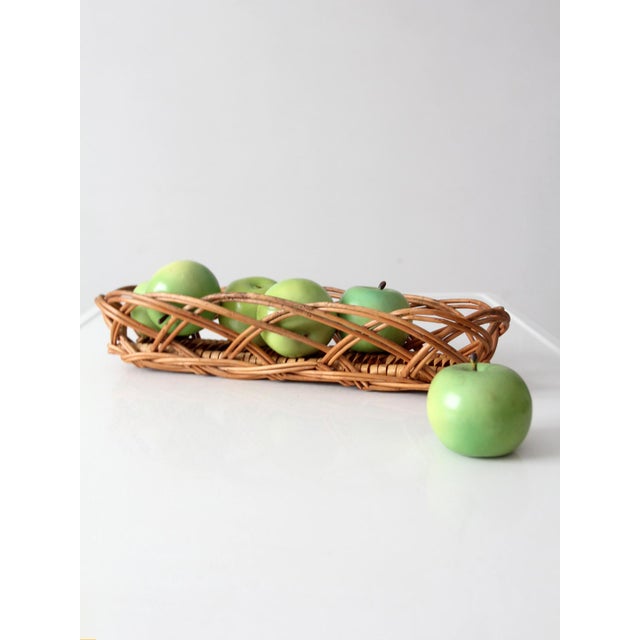 A vintage wicker bread basket with a long, low profile and an expressive looping weave. The warm honey-brown wicker and...