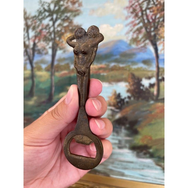 A vintage cast iron bottle opener featuring a sculptural figural design of two nude female forms conjoined at the torso....