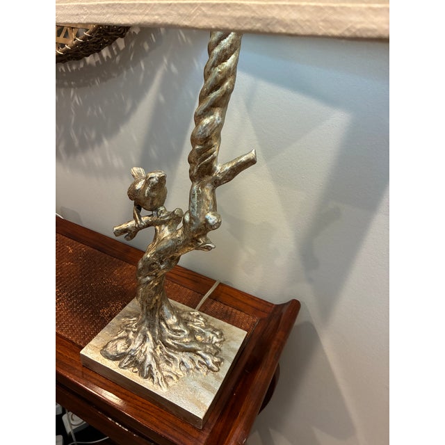 Beautiful nature-inspired table lamp featuring a sculpted songbird perched on a twisted tree branch. The lamp has an...