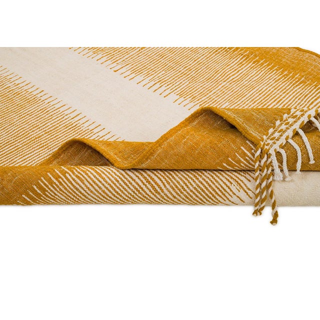 A bold mustard yellow border frames a quiet ivory center in this handwoven flatweave, its fringed edges signaling honest,...