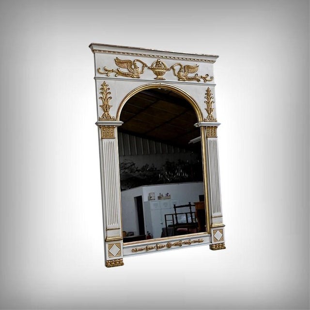 This Directoire-style trumeau mirror is distinguished by its painted frame enhanced with delicate gilt ornaments, which...