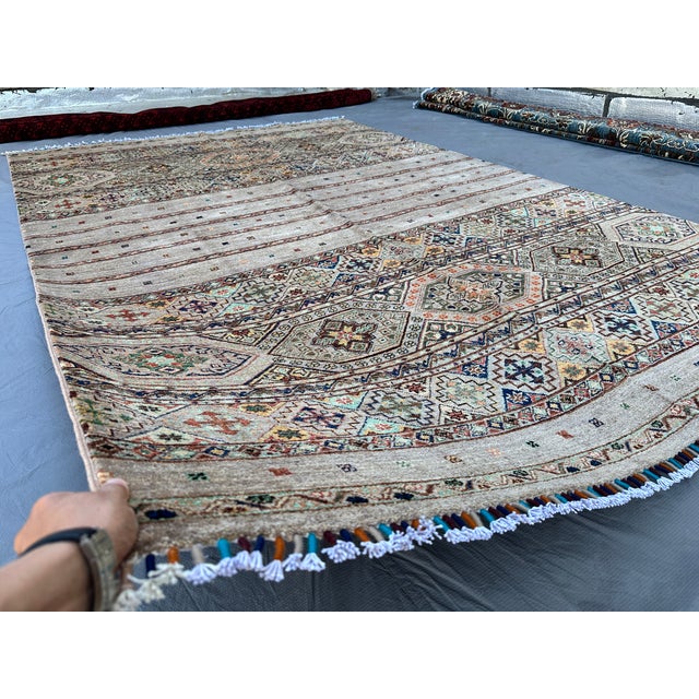 This contemporary Khorjin rug features alternating horizontal bands of soft striped sections and diamond-lattice...