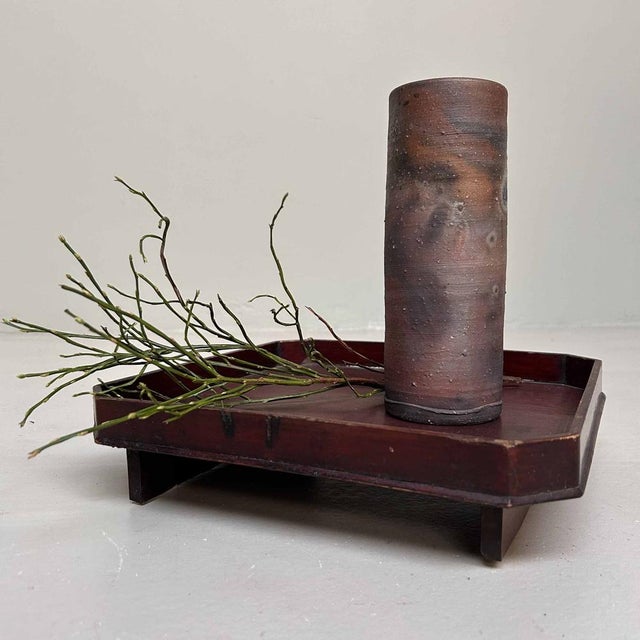This cylindrical ikebana vase distinguishes itself with a unique earthy color palette, formed during the traditional wood-...