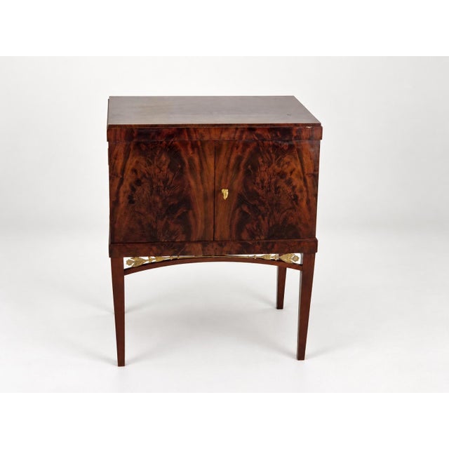 An elegant cabinet on four slender legs, combining Biedermeier simplicity with Empire-inspired decorative details. The...