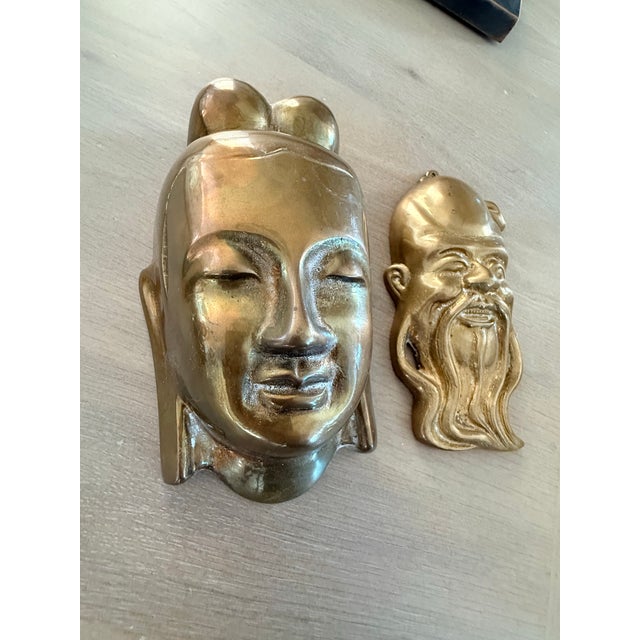 Two vintage brass masks. One looks like a Tibetan woman and the other is a holy man.