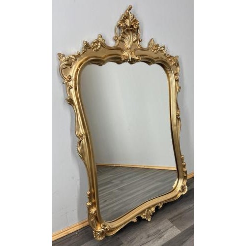 This Vintage French wall mirror features an ornate, flowing frame with elegant scrollwork and a decorative crest, creating...